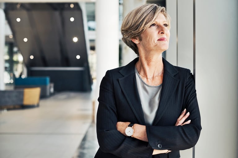 Cropped shot of a confident mature businesswoman looking away thoughtfully while standing with her arms folded in a modern office