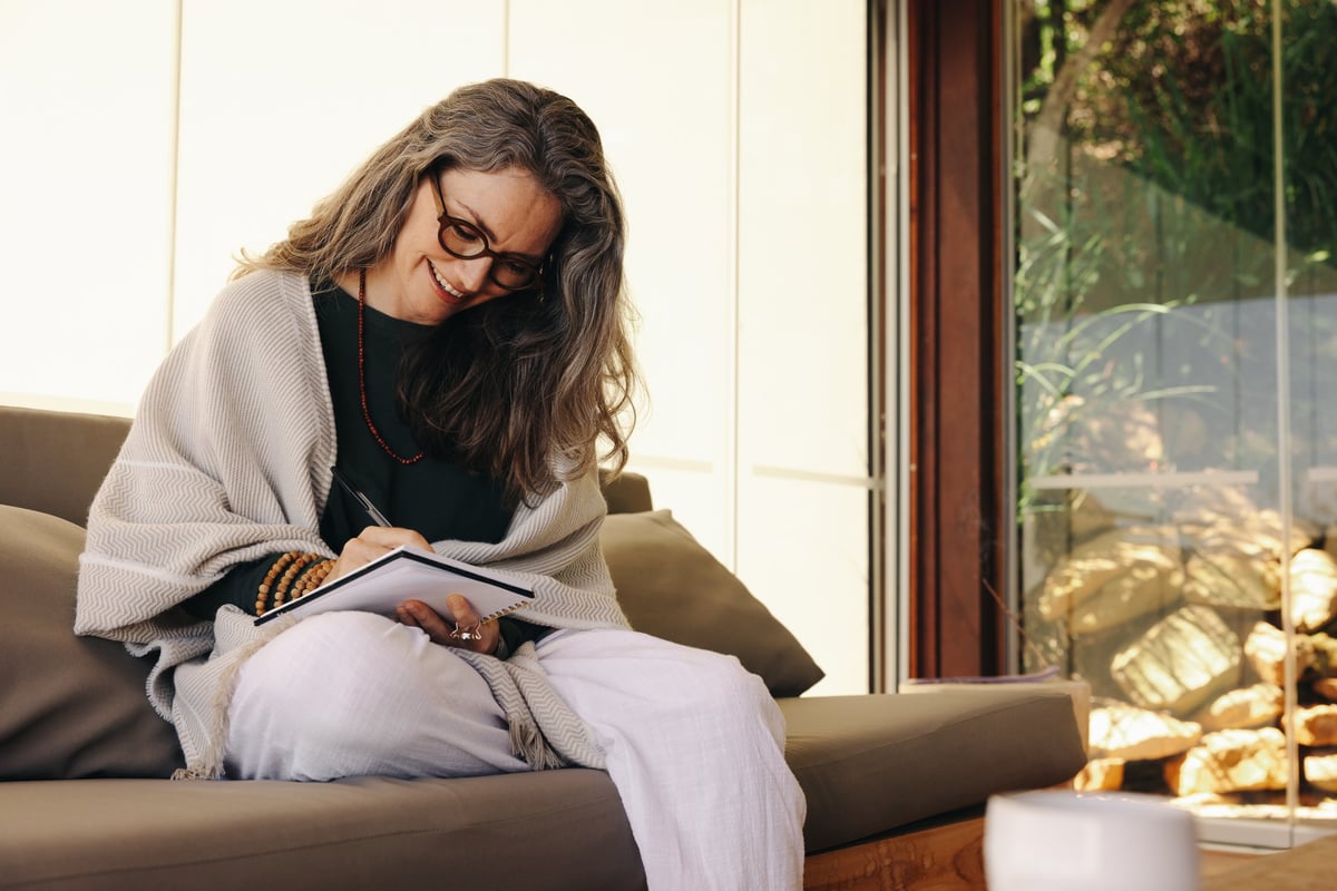 Mature woman in her 50s smiling while journaling at home, embracing midlife renewal and rediscovery