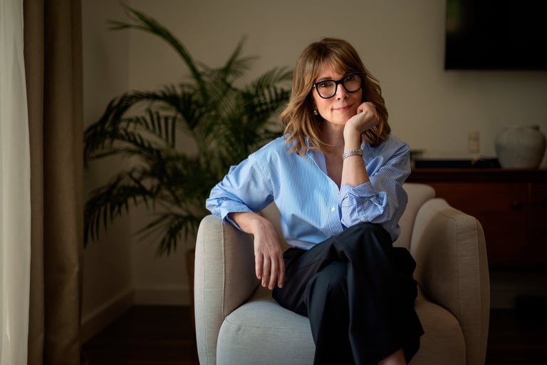 Shot of beautiful middle aged woman sitting in a cozy armchair in her modern home. Confident female wearing shirt and pants and smiling at camera.