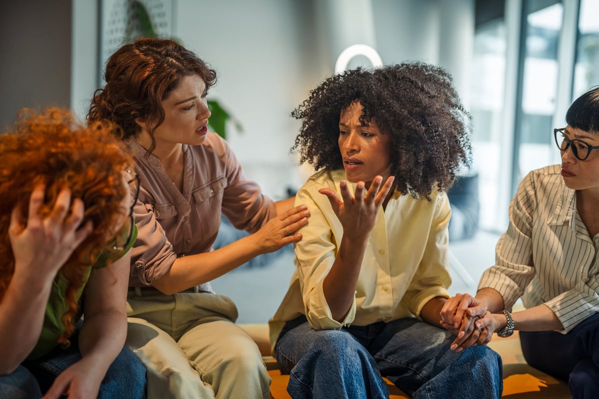 Diverse group of women offering comfort and understanding to a distressed friend, showing empathy and trust during a mental health support meeting or therapy session